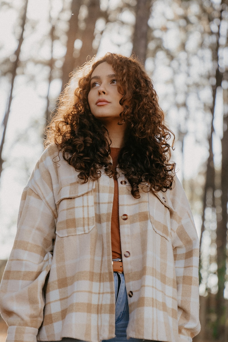a woman with curly hair standing in the woods